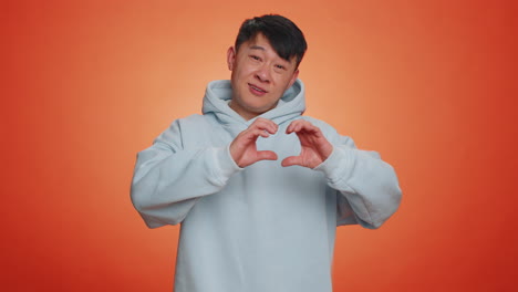 Smiling-chinese-man-makes-heart-gesture-demonstrates-love-sign-expresses-good-feelings-and-sympathy