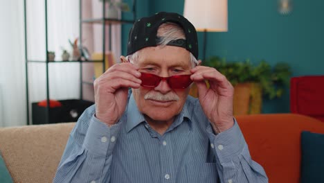 Stylish-grandpa-in-marijuana-cap-hat,-wearing-red-sunglasses,-looking-at-camera-with-charming-smile