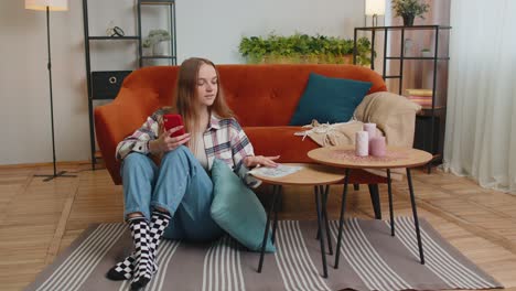 Smiling-happy-young-woman-counting-money-cash-and-use-mobile-phone-calculate-domestic-bills-at-home