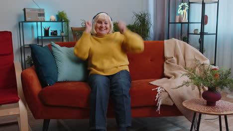 Happy-grandmother-old-woman-in-wireless-headphones-relaxing-on-sofa-at-home-listening-favorite-music