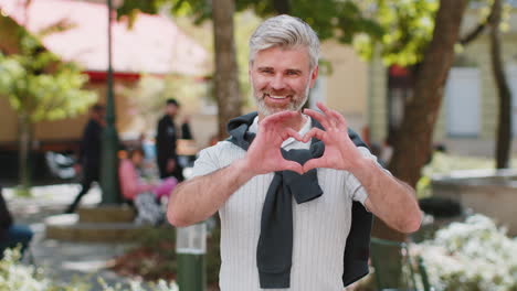 Mature-man-makes-symbol-of-love-showing-heart-sign-to-camera-express-romantic-positive-feelings