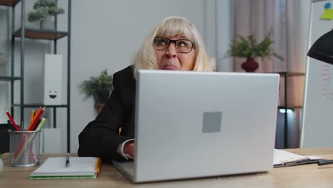 Senior-mature-older-business-woman-hiding-behind-laptop-computer,-making-funny-face,-fooling-around