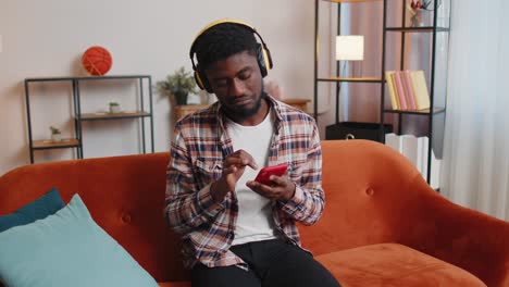 Joven-Afroamericano-Con-Auriculares-Escuchando-Música-Bailando,-Cantando-En-La-Sala-De-Estar-De-Casa