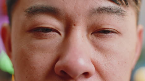 Close-up-macro-portrait-of-asian-man-face-smiling,-brown-gauy-eyes-looking-at-camera-blink-wink