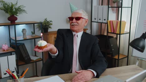 Un-Hombre-De-Negocios-Senior-Celebrando-Un-Cumpleaños-Solitario-En-El-Cargo,-Soplando-Una-Vela-En-Un-Pastel-Pequeño-Pidiendo-Un-Deseo