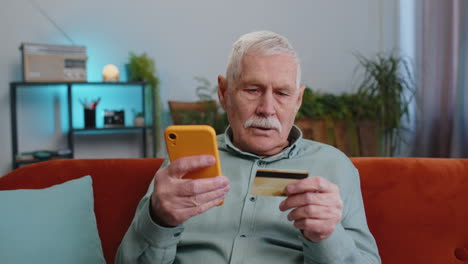 Grandfather-man-using-credit-bank-card-and-smartphone,-transferring-money-purchases-online-shopping