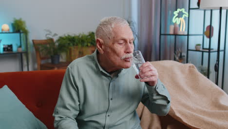 Thirsty-grandfather-man-sitting-at-home-holding-glass-of-natural-aqua-make-sips-drinking-still-water