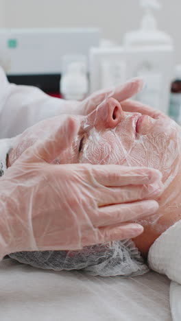 Esteticista-Aplicando-Mascarilla-De-Crema-Hidratante-Exfoliante-En-La-Cara-De-Una-Mujer-Joven-Para-Rehidratar-La-Piel-De-La-Cara