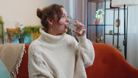 Thirsty-young-woman-sitting-at-home-holding-glass-of-natural-aqua-make-sips-drinking-still-water