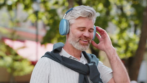 Relaxed-smiling-mature-bearded-man-listening-energetic-disco-rock-n-roll-music-dancing-outdoors