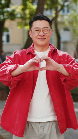 Asian-man-makes-symbol-of-love,-showing-heart-sign-to-camera,-express-romantic-positive-feelings