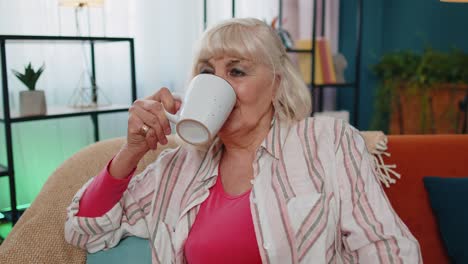 Senior-stylish-old-grandmother-woman-sitting-on-couch-relaxing-at-home-drinking-enjoy-tea-or-coffee