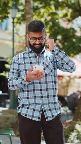 Indian-man-use-mobile-smartphone-celebrating-win-good-message-news-outdoors-on-urban-city-street