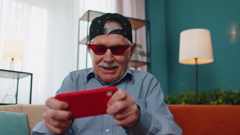 Worried-funny-senior-old-grandfather-man-playing-shooter-online-video-games-on-mobile-phone-at-home