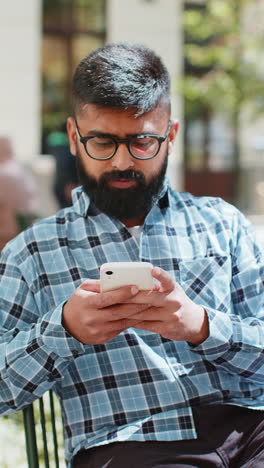 El-Hombre-Indio-Usa-Un-Teléfono-Inteligente-Escribiendo-Mensajes-De-Texto-Navegando-Por-Internet-Terminando-El-Trabajo-Mirando-La-Cámara