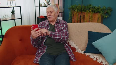 Senior-old-grandparent-works-on-mobile-phone,-sends-messages,-makes-online-purchases-at-home-sofa