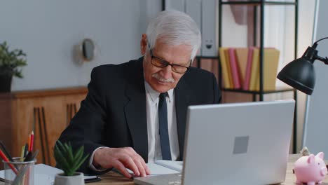 Senior-business-office-man-analyzes-financial-charts-celebrate-success-win-at-home-workplace-desk