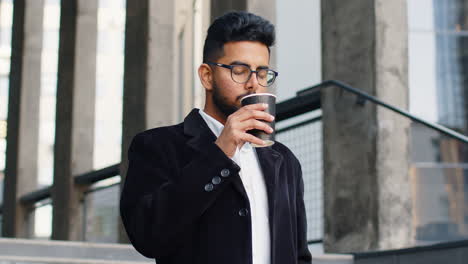 Happy-Indian-business-man-enjoying-morning-coffee-hot-drink-relaxing-taking-a-break-in-downtown-city