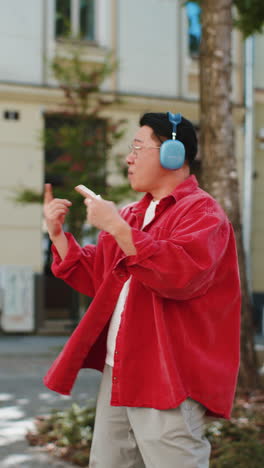 Fröhlicher-Asiatischer-Mann,-Der-In-Kabellosen-Kopfhörern-Tanzt-Und-Auf-Der-Stadtstraße-Seine-Lieblingsmusik-Hört