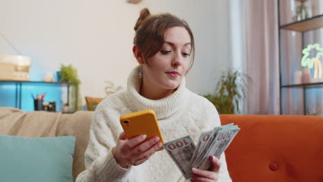 Mujer-Joven-Sonriente-Y-Feliz-Contando-Dinero-En-Efectivo,-Uso-De-Ingresos-Por-Teléfono-Inteligente,-Ahorra-Lotería-Y-Gana-El-Presupuesto-En-Casa