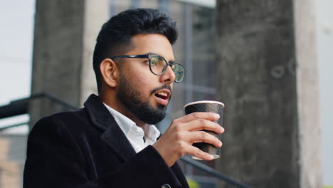 Happy-Indian-business-man-enjoying-morning-coffee-hot-drink-relaxing-taking-a-break-in-downtown-city