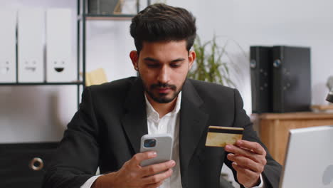 Business-man-making-online-purchase-payment-shopping-with-credit-bank-card-and-smartphone-at-office