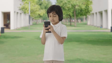 Niño-Indio-Enviando-Mensajes-De-Texto-A-Alguien-Por-Teléfono-En-El-Parque