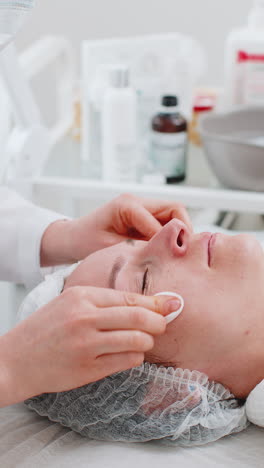 Cosmetologist-doctor-wipes-woman-face-and-neck-cleaning-procedure-with-cotton-wipes-in-beauty-clinic