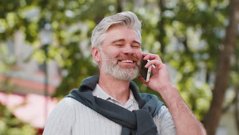 Mature-tourist-man-having-remote-conversation-online-talk-by-smartphone-unexpected-good-news-gossip