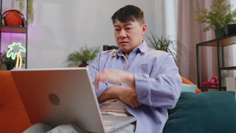 Asian-middle-aged-man-use-laptop-surprised-by-bad-news,-fortune-loss,-fail,-lottery-results-at-home