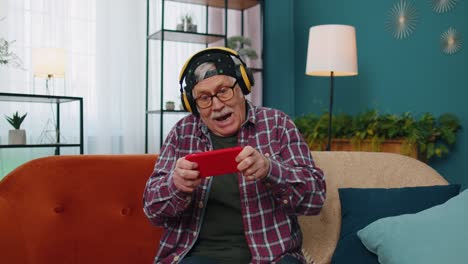 Worried-funny-senior-old-grandfather-man-playing-racing-online-video-games-on-mobile-phone-at-home