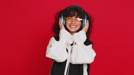 Woman-listening-music-on-headphones,-dancing-disco-fooling-around-having-fun-on-red-background