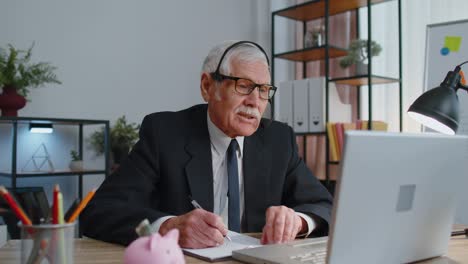 Un-Hombre-De-Negocios-De-Alto-Nivel-Usa-Auriculares-Inalámbricos-Haciendo-Videollamadas-De-Conferencia-En-Una-Computadora-Portátil,-Agente-Del-Centro-De-Llamadas