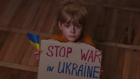 Afraid-Ukrainian-girl,-inscription-massage-Stop-War-In-Ukraine-hiding-from-bombing-attack-at-home