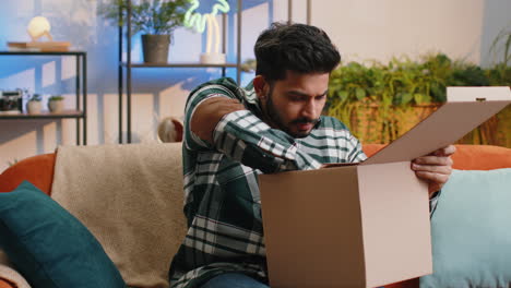 Happy-indian-man-shopper-unpacking-cardboard-box-delivery-parcel-online-shopping-purchase-at-home