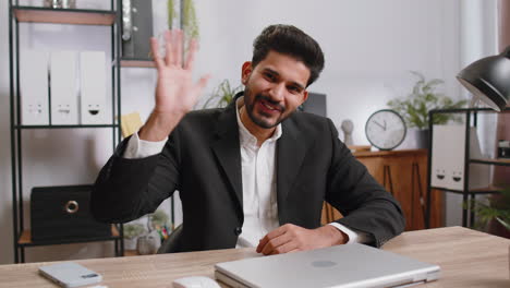 Hombre-De-Negocios-Trabajando-En-Una-Computadora-Portátil-Sonriendo-Amablemente-A-La-Cámara-Y-Saludando-Con-Las-Manos-En-La-Oficina