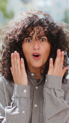 Young-woman-looking-surprised-at-camera-shocked-by-sudden-win-good-victory-news,-wow-in-city-street