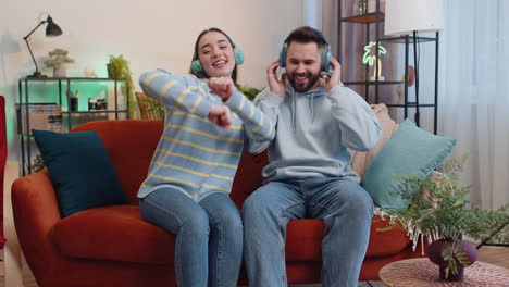 Hombre-De-Familia-Mujer-Con-Auriculares-Inalámbricos-Bailando-Escuchando-Música-Rock-N-Roll-Favorita-En-El-Sofá-De-Casa