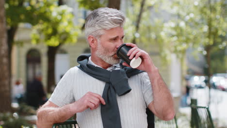 Mature-man-enjoying-morning-coffee-hot-drink-relaxing-taking-a-break-sitting-on-cafe-chair-on-street