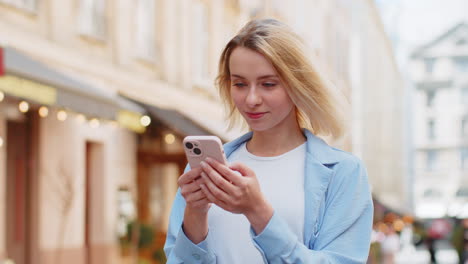 Mujer-Feliz-Usando-Un-Teléfono-Inteligente-Escribiendo-Mensajes-De-Texto-De-Aplicaciones-De-Redes-Sociales-Mensajes-De-Correo-Electrónico-En-Las-Calles-De-La-Ciudad