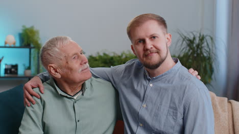 Retrato-De-Un-Abuelo-Maduro-Con-Un-Nieto-Adulto-Joven-Sonriendo-Feliz-Abrazandose-En-Casa