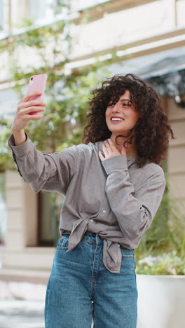 Young-woman-blogger-taking-selfie-on-smartphone-video-call-online-with-subscribers-on-city-street