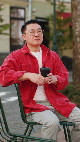 Happy-Asian-man-enjoying-drinking-morning-coffee-hot-drink,-relaxing,-taking-a-break-on-city-street