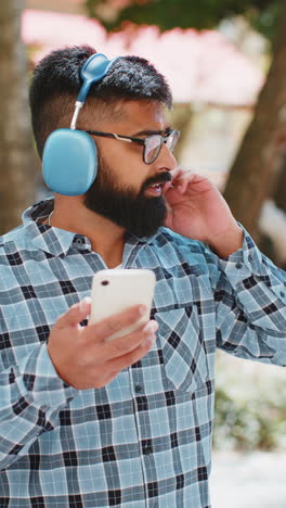 Happy-Indian-man-dancing-in-wireless-headphones-listening-favorite-energetic-music-on-city-street