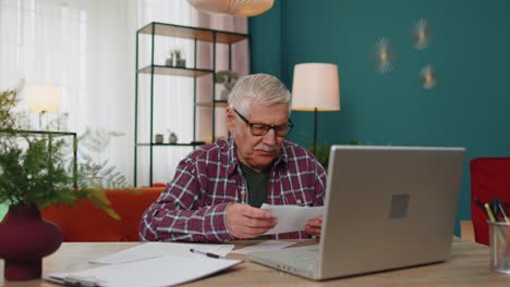 Grandfather-calculating-household-bills-bank-loan-online-domestic-expenditures-payment-on-laptop-app