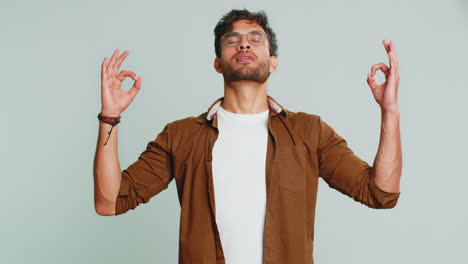 Indian-man-meditating-breathes-deeply-with-mudra-yoga-gesture,-eyes-closed,-taking-a-break,-relax