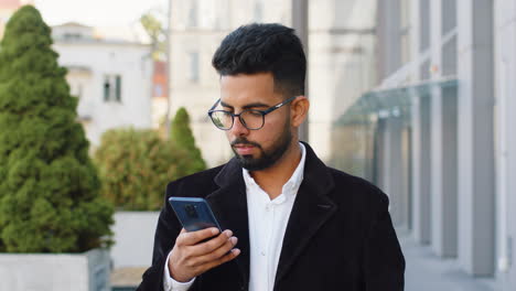 Lächelnder-Geschäftsmann,-Der-Sein-Smartphone-Benutzt-Und-Textnachrichten-Eintippt-Und-Auf-Der-Stadtstraße-Online-Chattet