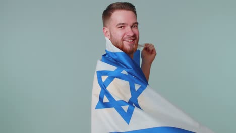 Man-waving-and-wrapping-in-Israel-national-flag,-celebrating-Independence-day-on-gray-background