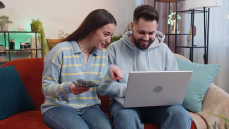 Familia-Feliz-Y-Sonriente-Contando-Dinero-En-Efectivo-Y-Usando-Una-Computadora-Portátil-Para-Calcular-Los-Ingresos-Domésticos-En-Casa