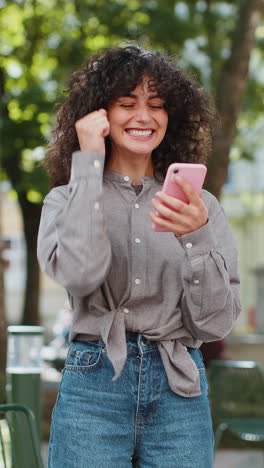 Mujer-Caucásica-Utiliza-Un-Teléfono-Inteligente-Móvil-Celebrando-Ganar-Buenas-Noticias-Al-Aire-Libre-En-Las-Calles-De-La-Ciudad